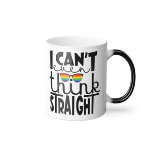 Könnte beinhalten: Eine weiße Keramik-Kaffeetasse mit schwarzem Henkel. Die Tasse hat ein schwarzes Design mit dem Text "Ich kann nicht mal gerade denken" und einer regenbogenfarbenen Sonnenbrille in der Mitte des Textes.