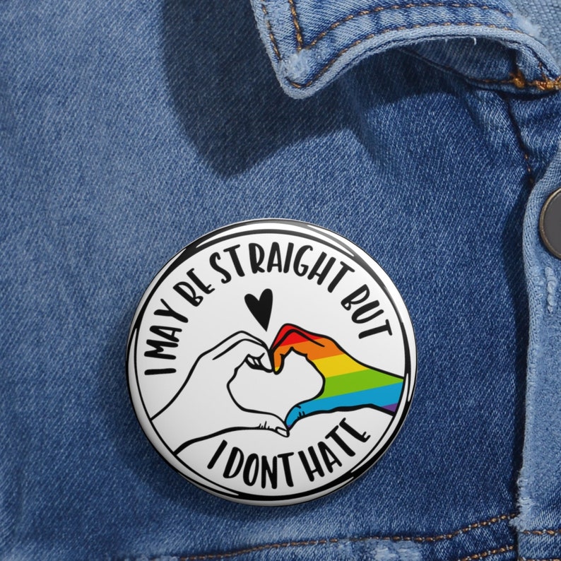 May include: A white button with black text and a rainbow heart design. The text reads "I may be straight but I don't hate".
