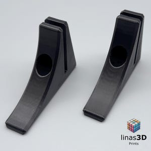 May include: Two black 3D-printed stands with a curved base and a vertical slot at the top. Each stand has a circular cutout near the centre. The stands are designed to hold an item upright. The logo "linas3D Prints" is in the bottom right corner.
