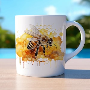 Könnte beinhalten: Weiße Keramiktasse mit einer Aquarell-Illustration einer Biene auf einer Wabe. Die Biene ist gelb und schwarz mit braunen Streifen. Die Wabe ist gelb und braun mit einem Aquarelleffekt. Der Hintergrund ist weiß mit ein paar gelben und braunen Aquarellspritzern.