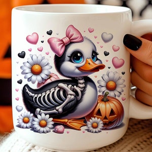Könnte beinhalten: Eine weiße Keramiktasse mit einem schwarz-weißen Cartoon-Skelett-Entchen, das eine rosa Schleife trägt. Das Entchen hält eine kleine Halloween-Kürbislaterne. Die Tasse ist von rosa Herzen und weißen Gänseblümchen umgeben.