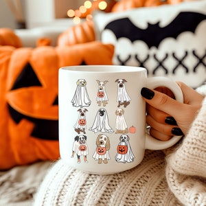 Pu&ograve; includere: Tazza in ceramica bianca con un design a tema Halloween. Il design include illustrazioni di varie razze di cani vestiti da fantasmi, alcuni con lanterne a forma di zucca. La tazza ha un manico grande.