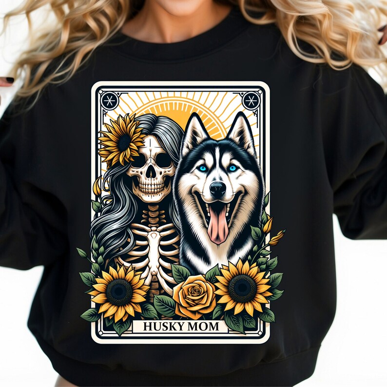 Puede incluir: Sudadera negra con un dise&ntilde;o gr&aacute;fico de una mujer esqueleto con girasoles y un perro husky. El texto "HUSKY MOM" est&aacute; impreso debajo de la imagen.