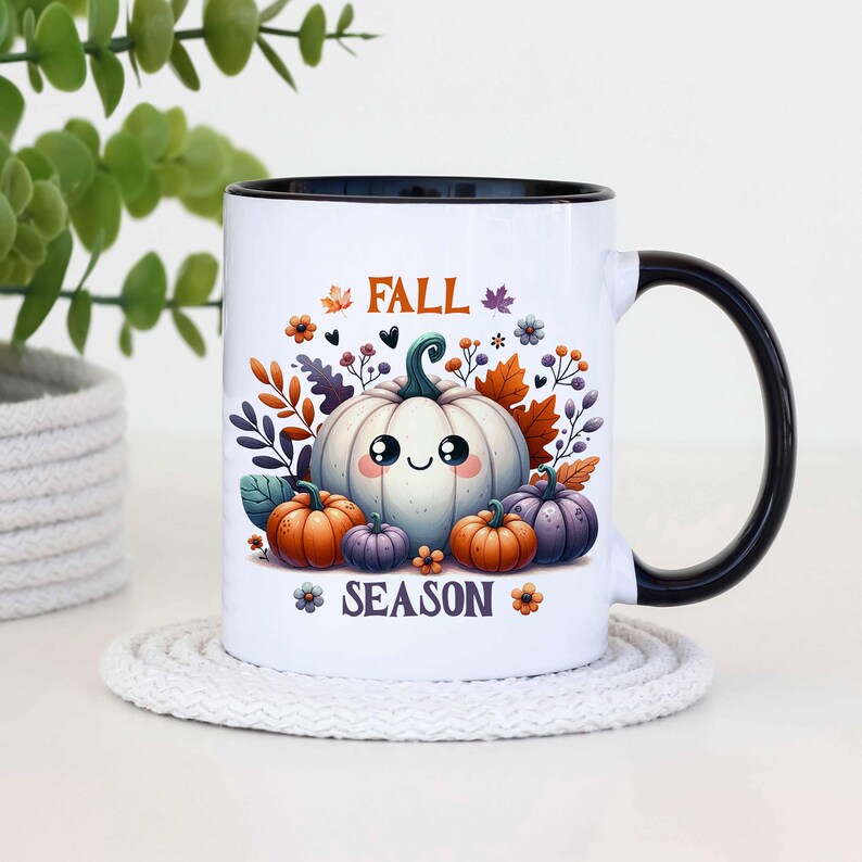 May include: White ceramic mug with a black interior and handle. The mug features a cute cartoon pumpkin design with the words "FALL SEASON" in orange and purple. The design includes pumpkins, leaves, and flowers.