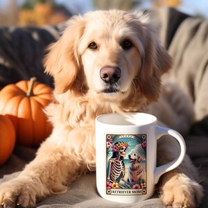 以下が含まれることがあります： ビーチでスケルトン犬とゴールデンレトリバーのカラフルなイラストが描かれた白いセラミック製のコーヒーカップ。カップの下部に「RETRIEVER MOM」の文字が印刷されています。