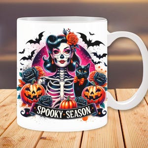 May include: White ceramic mug with a colorful illustration of a skeleton woman with a black cat, pumpkins, and bats. The text "Spooky Season" is printed on the mug.