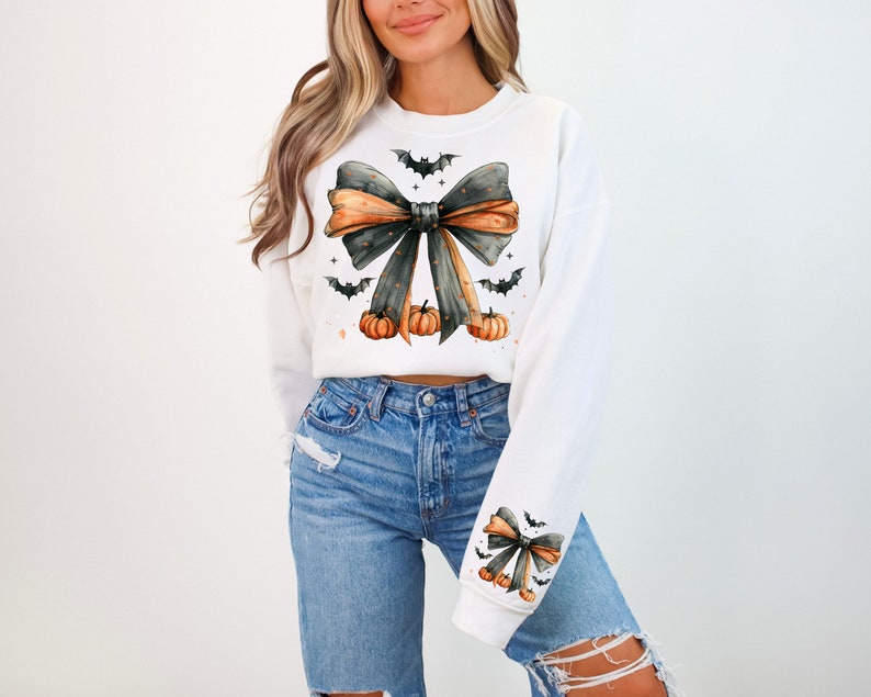 May include: White sweatshirt with a black and orange bow, bats, and pumpkins. The bow has a black and white polka dot pattern.