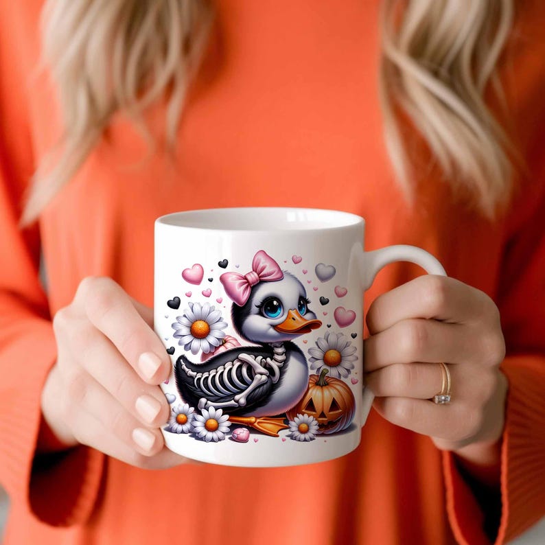 May include: White ceramic mug with a black and white cartoon duck with a pink bow and a skeleton design. The duck is holding a small orange pumpkin with a jack-o'-lantern face. The mug is surrounded by white daisies and pink hearts.