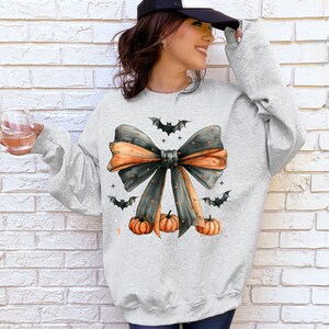 May include: A gray sweatshirt with a black and orange bow with bats and pumpkins. The bow has white polka dots.