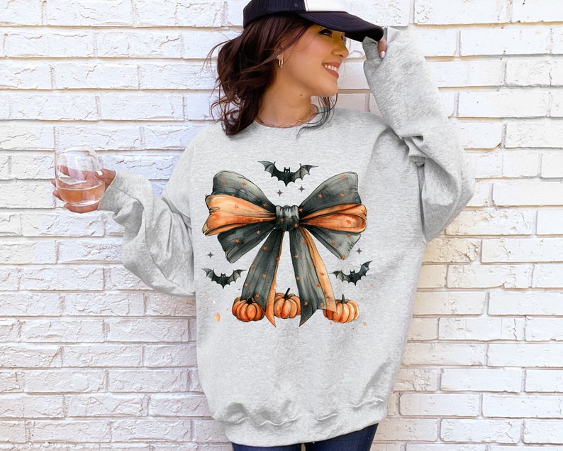 May include: A gray sweatshirt with a black and orange bow with bats and pumpkins. The bow has white polka dots.