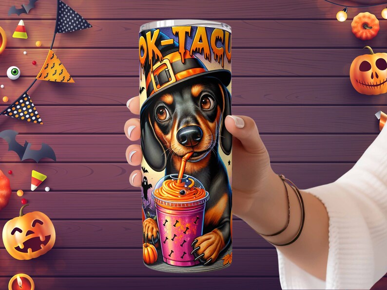 Może przedstawiać: Czarny i brązowy szczeniak rasy dachshund w czarnym kapeluszu czarownicy trzymający r&oacute;żowy i pomarańczowy nap&oacute;j na Halloween. Na kubku widnieje napis "Boo-Tacular".
