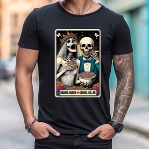 May include: A black t-shirt with a graphic of two skeletons dressed as a bride and groom eating cereal. The text "Drama Queen Cereal Killer" is below the skeletons.
