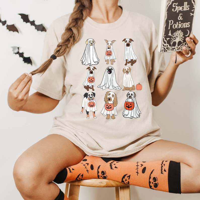 Pu&ograve; includere: T-shirt beige con un design a tema Halloween. La maglietta presenta illustrazioni di varie razze di cani vestiti da fantasmi, alcuni con secchi a forma di zucca. Il design &egrave; giocoso e festoso, perfetto per la stagione spettrale.