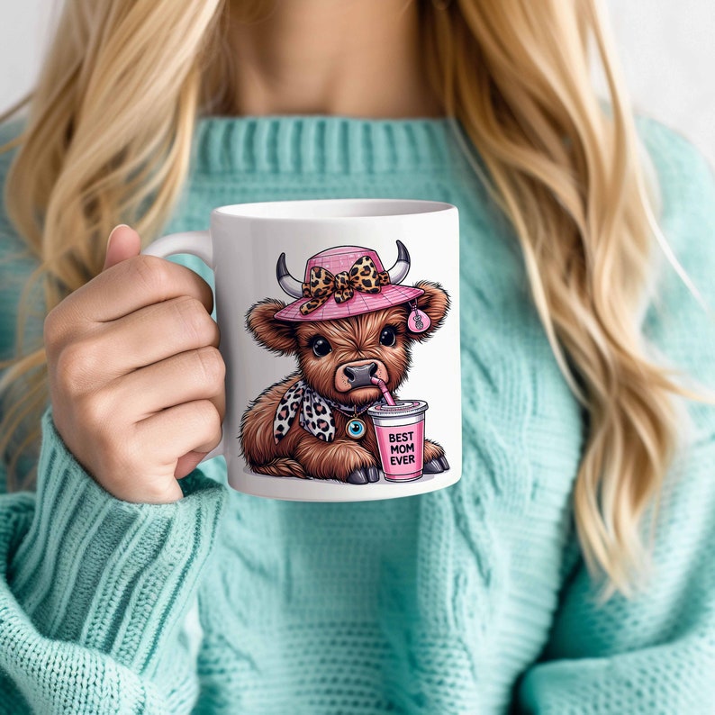 May include: White ceramic mug with a brown and white Highland cow wearing a pink hat with a leopard print bow and drinking from a pink cup that says "Best Mom Ever".