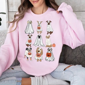 Pu&ograve; includere: Una felpa rosa chiaro con un design a tema Halloween. Il design include illustrazioni di varie razze di cani vestiti da fantasmi, ognuno con una lanterna di zucca. La felpa &egrave; uno stile casual e confortevole.