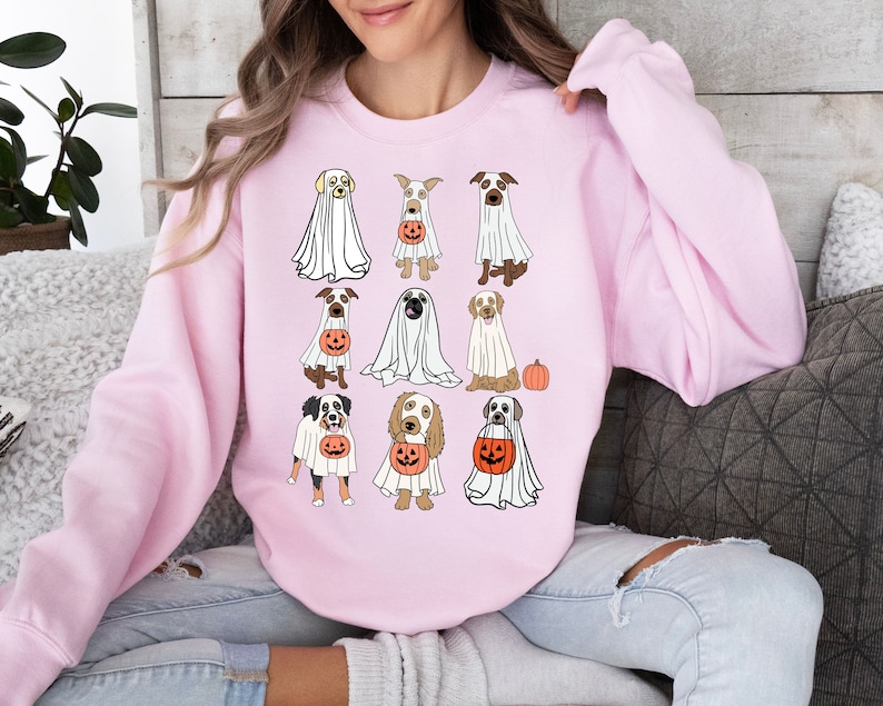 Pu&ograve; includere: Una felpa rosa chiaro con un design a tema Halloween. Il design include illustrazioni di varie razze di cani vestiti da fantasmi, ognuno con una lanterna di zucca. La felpa &egrave; uno stile casual e confortevole.