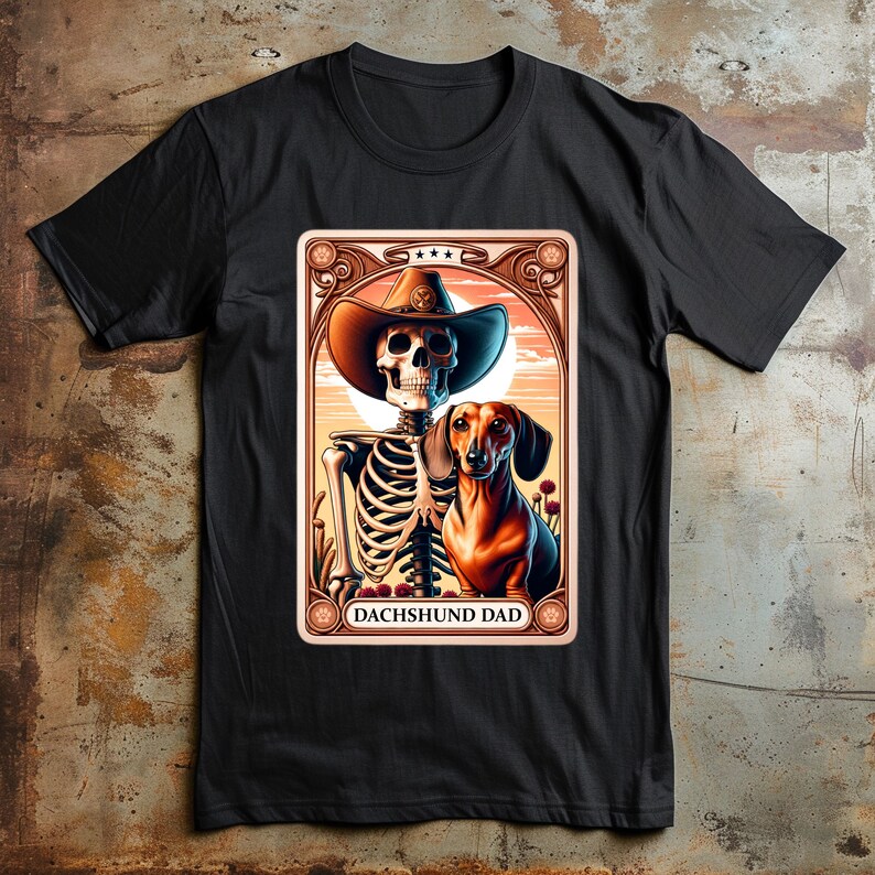 Op de afbeelding: Een zwart T-shirt met een afbeelding van een skelet dat een cowboyhoed draagt en een teckel vasthoudt. De afbeelding is in vintage stijl met een gouden frame en de tekst "Dachshund Dad".