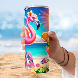 May include: A pink flamingo with a flower in its hair stands on a beach with a blue sky and ocean in the background. The tumbler has a colorful design with flip flops, a beach umbrella, and a tropical drink.