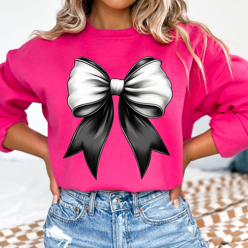 Puede incluir: Una sudadera rosa con un gran lazo negro y blanco en la parte delantera.