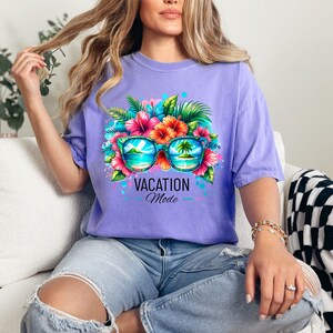 May include: A purple t-shirt with a graphic of sunglasses with tropical flowers and palm trees reflected in the lenses. The text "Vacation Mode" is printed below the sunglasses.