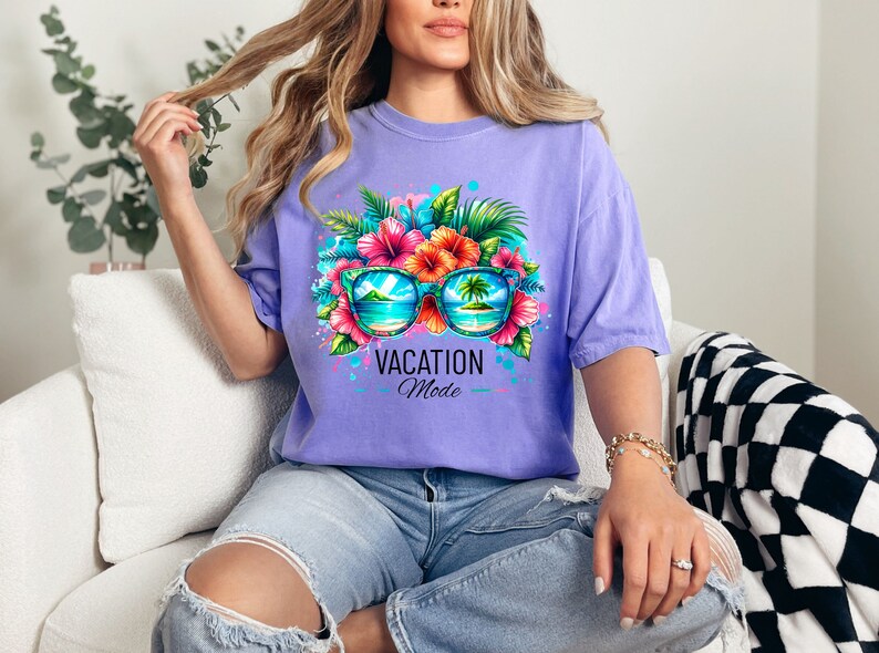 May include: A purple t-shirt with a graphic of sunglasses with tropical flowers and palm trees reflected in the lenses. The text "Vacation Mode" is printed below the sunglasses.