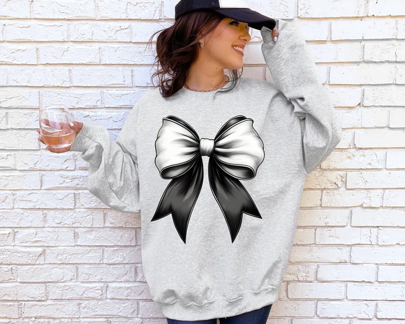 Puede incluir: Una sudadera gris con un gran lazo negro y blanco en la parte delantera.