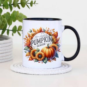 Pu&ograve; includere: Una tazza da caff&egrave; in ceramica bianca con bordo e manico neri. La tazza presenta un'illustrazione colorata di zucche, girasoli e foglie autunnali con il testo "Pumpkin Season".