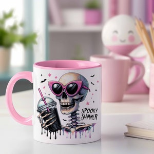 May include: Pink and white ceramic mug with a skeleton wearing sunglasses and holding a pink and black iced drink. The mug has the text "Spooky Summer" on it.