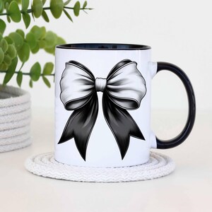 Puede incluir: Taza de cer&aacute;mica blanca con borde y asa negros. La taza presenta un dise&ntilde;o de lazo negro y blanco.