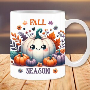 May include: White ceramic mug featuring a cartoon illustration of a smiling white pumpkin surrounded by orange, purple, and green pumpkins, leaves, and flowers. The words "FALL SEASON" are printed on the mug.
