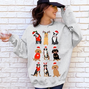 May include: A light gray sweatshirt featuring cartoon dogs in festive holiday attire. The dogs are wearing Santa hats, reindeer antlers, and Christmas lights. The sweatshirt is a crew neck style.