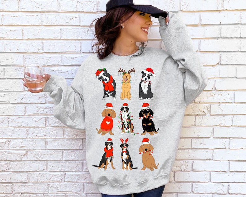 May include: A light gray sweatshirt featuring cartoon dogs in festive holiday attire. The dogs are wearing Santa hats, reindeer antlers, and Christmas lights. The sweatshirt is a crew neck style.