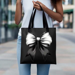 Puede incluir: Una bolsa de tela negra con un gran lazo blanco en la parte delantera. El lazo est&aacute; atado en un nudo y los extremos fluyen por los lados de la bolsa.