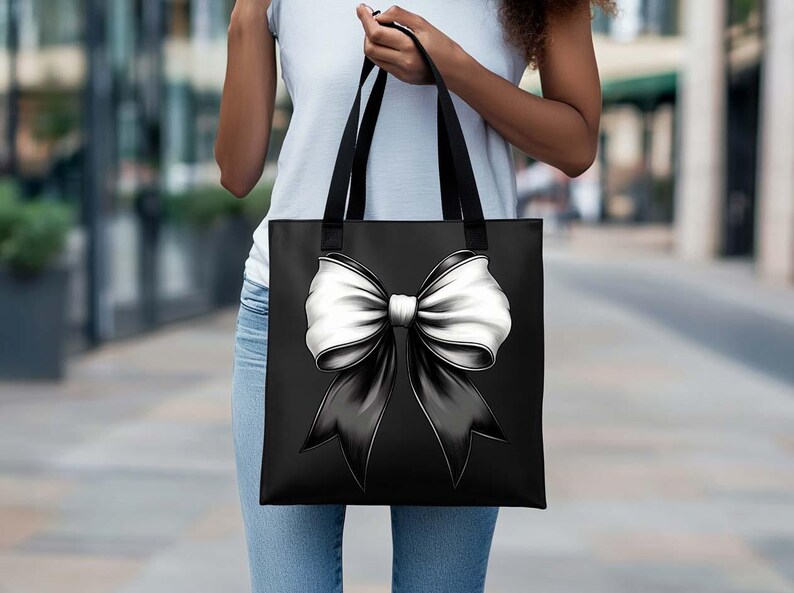 Puede incluir: Una bolsa de tela negra con un gran lazo blanco en la parte delantera. El lazo est&aacute; atado en un nudo y los extremos fluyen por los lados de la bolsa.