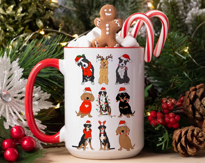 May include: A white ceramic mug with a red handle and rim, decorated with cartoon dogs in Christmas attire. The mug is filled with marshmallows, a gingerbread man, and candy canes. Festive holiday theme.