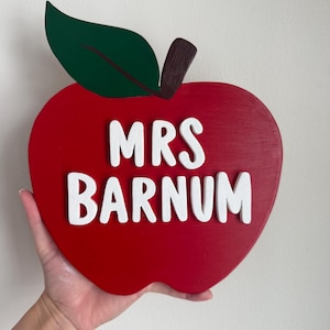 Peut inclure: Panneau en bois en forme de pomme rouge avec l'inscription "MRS BARNUM" en blanc. Il comporte une feuille verte et une tige marron. Un objet décoratif sur le thème de l'enseignant.
