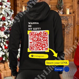 May include: Black hoodie with a red and white QR code on the back. The text "Wanna be my gift?" is above the QR code. The text "Instagram" is below the QR code. The text "Insert your LINK" is below the Instagram text. The text "Europe" is below the Insert your LINK text.