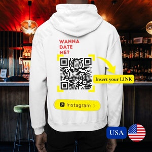 Op de afbeelding: Witte hoodie met de tekst "Wanna Date Me?" en een QR-code met de tekst "Insert your LINK" en "Instagram" onder de code.