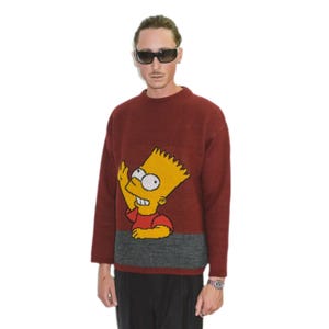 Könnte beinhalten: Ein weinroter Pullover mit einem grauen Band am unteren Rand. Der Pullover zeigt eine gelbe Comicfigur mit einem roten Shirt und schwarzen Haaren.