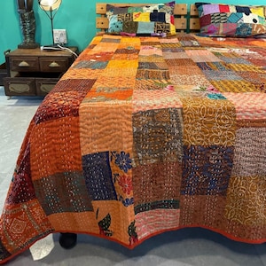 Puede incluir: Una colcha de retazos con una variedad de colores y patrones, incluyendo naranja, marrón y azul. La colcha está hecha de diferentes telas y está acolchada con una puntada corrida. La colcha está sobre una cama con dos almohadas, también hechas de tela de retazos.