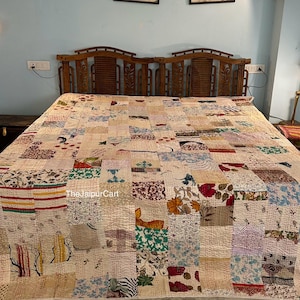 May include: A patchwork quilt with a variety of fabric patterns and colors, including floral, striped, and solid patches. The quilt is spread across a bed with a wooden headboard. The text "The Jaipur Cart" is visible on the quilt.