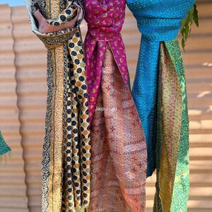 May include: Three patterned scarves hanging outside. The scarves display diverse designs, such as polka dots, floral patterns, and geometric shapes. Colours include blue, pink, yellow, and green. The scarves are made of a lightweight material.