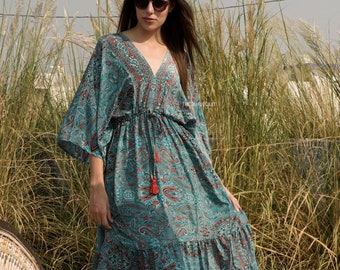 Könnte beinhalten: Ein langes, fließendes, blaugrünes Maxikleid mit Paisley-Muster und einem roten Quastenband in der Taille. Das Kleid hat einen V-Ausschnitt und 3/4-Ärmel.