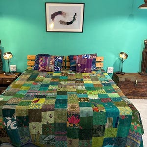 Puede incluir: Una colcha de retazos verde y azul con una variedad de patrones y colores. La colcha est&aacute; en una cama con dos almohadas. La habitaci&oacute;n tiene una pared verde turquesa y un cuadro enmarcado en la pared.