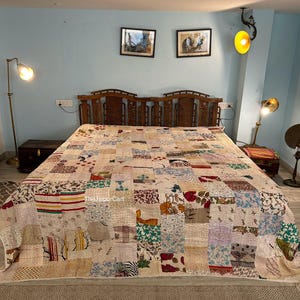 May include: A patchwork quilt with a variety of fabric patterns and colors, including floral, striped, and solid patches. The quilt is spread across a bed with a wooden headboard. The text "The Jaipur Cart" is visible on the quilt.