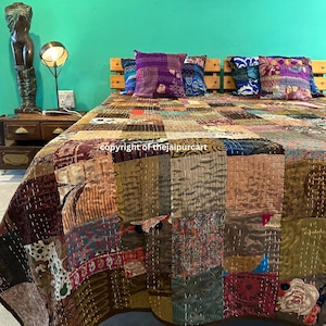 May include: A patchwork quilt with a variety of fabrics in shades of brown, beige, and red covers a bed. Four decorative pillows in purple, blue, and patterned fabrics rest against the wooden headboard. The room has a teal wall.