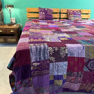 Puede incluir: Una colcha de retazos de color morado y azul con una variedad de patrones florales y geom&eacute;tricos. La colcha est&aacute; hecha de tela kantha y est&aacute; cosida a mano. Est&aacute; colocada sobre una cama con dos fundas de almohada a juego.
