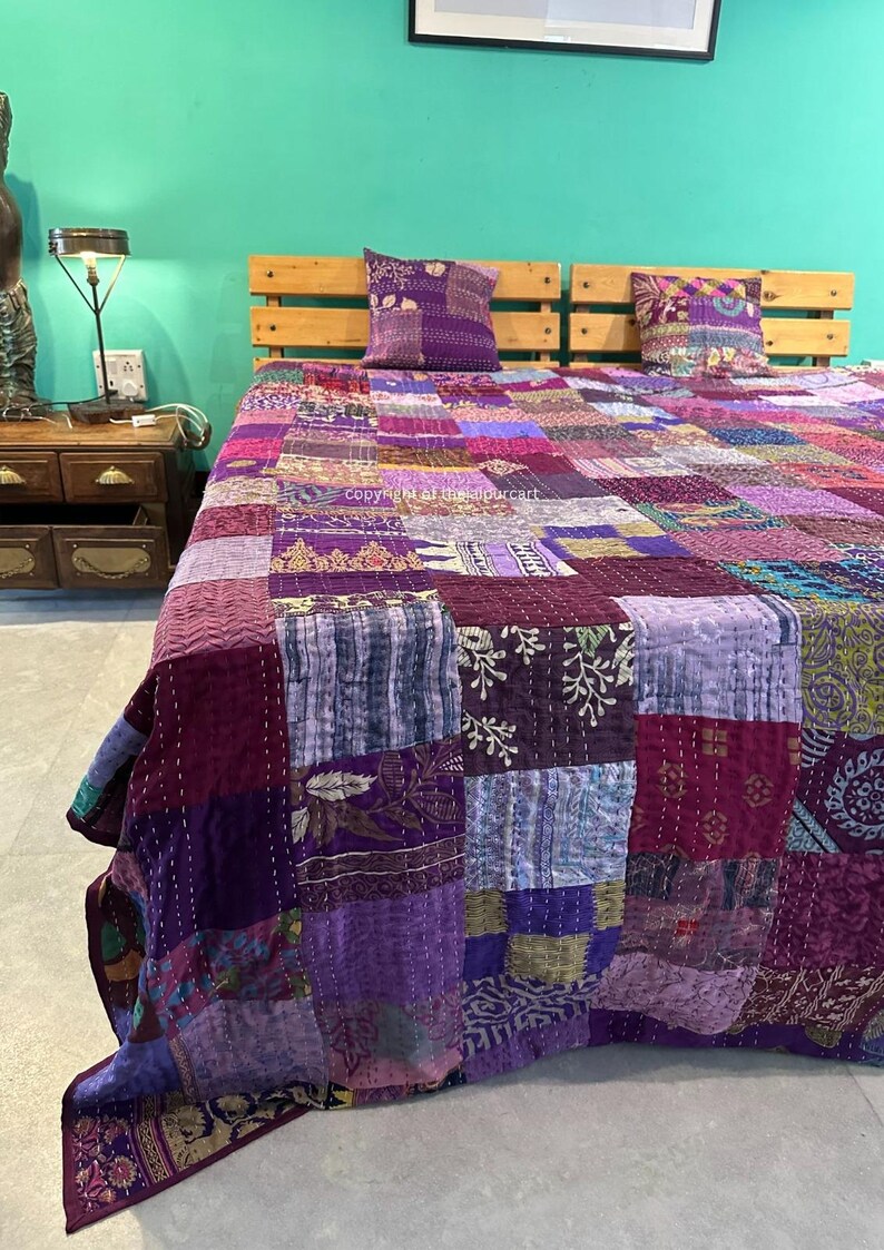 Puede incluir: Una colcha de retazos de color morado y azul con una variedad de patrones florales y geom&eacute;tricos. La colcha est&aacute; hecha de tela kantha y est&aacute; cosida a mano. Est&aacute; colocada sobre una cama con dos fundas de almohada a juego.