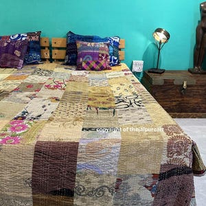 Könnte beinhalten: Eine Patchwork-Quiltdecke mit verschiedenen Stoffmustern und -farben, darunter Blumen- und geometrische Designs. Die Quiltdecke liegt auf einem Bett mit dekorativen Kissen und einem hölzernen Kopfteil. Die Farbpalette umfasst Beige, Braun und Lila.