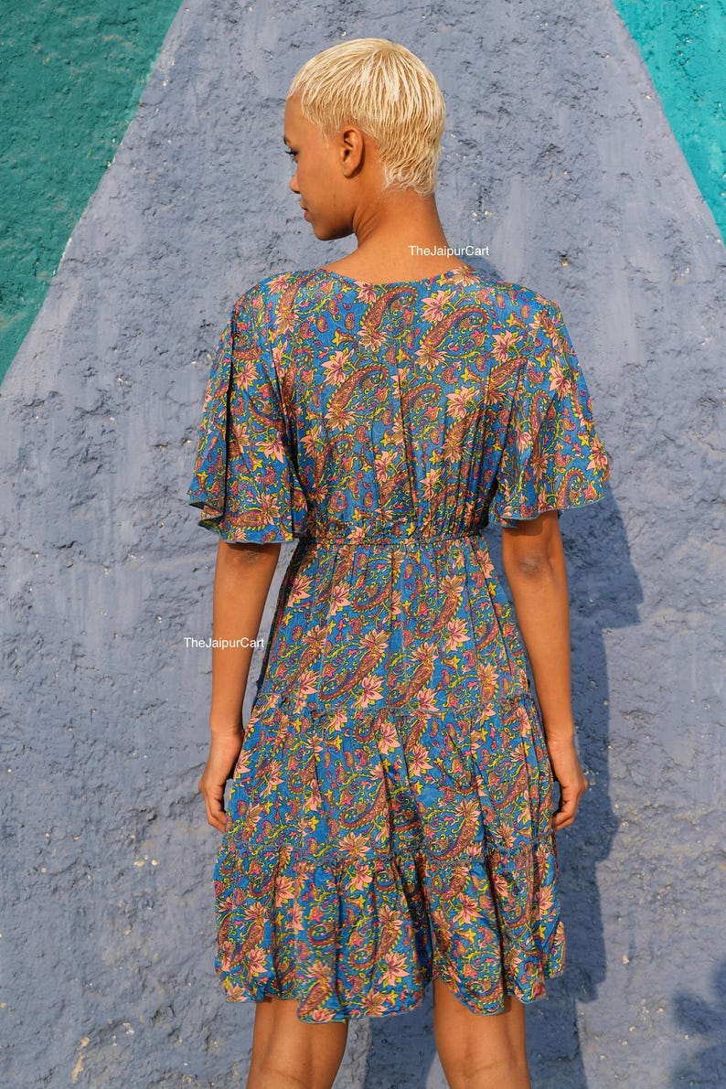 K&ouml;nnte beinhalten: Blaues Paisley-Kleid mit kurzen &Auml;rmeln und einem Stufenrock. Das Kleid hat einen V-Ausschnitt und eine betonte Taille. Der Stoff hat ein Blumen- und Paisley-Muster in Rosa-, Gelb- und Blaut&ouml;nen. The Jaipur Cart ist auf dem Kleid aufgedruckt.